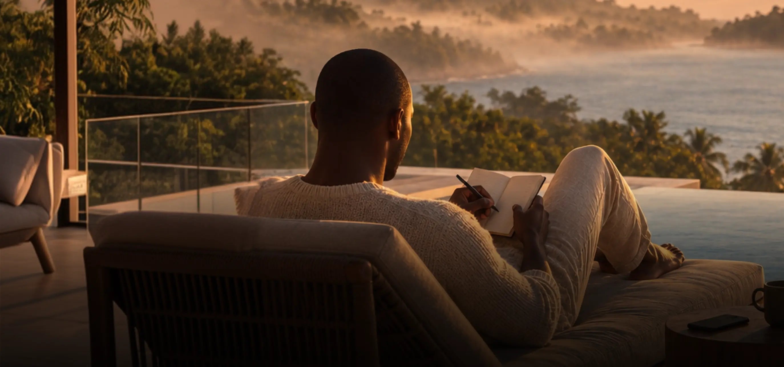 A man writing in a notebook by the sea at sunrise